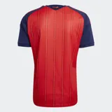 Camiseta de fútbol Adidas de la selección de España, primera equipación 2026. Diseño en color rojo con mangas y detalles en azul, con rayas verticales sutiles y el escudo de la selección en el pecho.