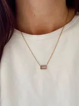 Collar de cadena fina dorada con un dije rectangular que contiene una piedra de cristal en tono rosado.