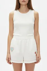 Short ancho de tiro alto confeccionado en mezcla de lino y viscosa, de color blanco. Presenta detalles bordados de un corazón y frutillas en la parte frontal, además de una línea ondulada decorativa en contraste en el ruedo. Cuenta con cintura elástica.