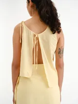 Blusa sin mangas de color amarillo claro, con diseño asimétrico en capas y detalles de tirantes finos en los hombros.
