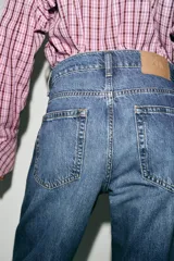 Jeans de tiro alto con diseño barrel, caracterizado por una silueta curvada y holgada en la zona de los muslos y rodillas, estrechándose hacia el tobillo. Cuenta con cinco bolsillos y cierre frontal con cremallera y botón.