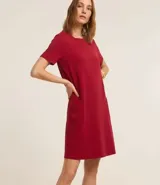 Vestido corto marrón oscuro, estilo camiseta, con escote redondo, mangas cortas y bolsillos laterales. El bajo es redondeado.