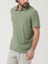 Remera tipo polo de manga corta en color verde sage, con textura jaspeada. Presenta un bolsillo frontal en el pecho, cuello clásico y cierre frontal con botones.
