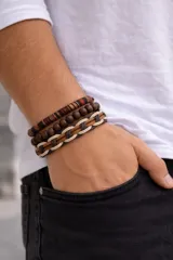 Set de tres pulseras para hombre. Una pulsera de cuentas negras mate con detalles de piedras verdes y cuentas metálicas plateadas. Dos pulseras de cuero sintético negro con diferentes texturas. Una pulsera de tela trenzada con diseño geométrico en blanco y negro.