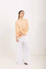 Blusa de diseño cuadrillé en tonos beige y verde claro, de corte amplio y mangas largas abullonadas con puños elastizados con volados. Cuenta con cuello mao y una abertura frontal parcial con botones.