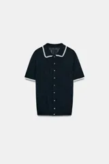 Chaqueta de punto de manga corta con cuello polo y cierre frontal de botones, en color negro con detalles de puntilla blanca en el cuello y los puños.