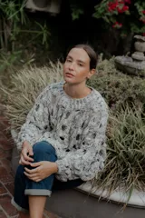 Buzo de tejido de punto calado con diseño de red, cuello redondo y mangas largas abullonadas. Presenta una textura jaspeada en tonos gris y blanco.