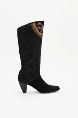 Bota de caña alta confeccionada en gamuza negra, con un diseño artesanal de parches en cueros texturizados y metalizados con motivos florales. Presenta un taco cónico y punta almendrada.