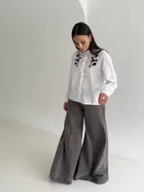 Camisa blanca de manga larga con cuello mao, cierre frontal de botones y detalle de volado. Presenta bordados florales en color marrón chocolate en la parte superior delantera.