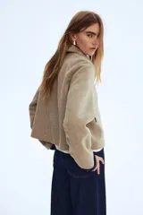 Campera corta de corte recto en color beige melange, con cuello camisero y cierre frontal mediante botones a contraste. Presenta dos bolsillos de parche con solapa en la parte delantera y cuenta con forro interior.