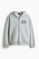 Campera con capucha de felpa gris, con cierre frontal completo, bolsillos tipo canguro y estampado tipográfico en el pecho. Presenta hombros caídos y puños acanalados.