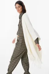 Ruana de tejido suave y envolvente en color blanco, con diseño de corte amplio y terminación de flecos en el ruedo.