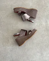 Sandalias de cuero vacuno color negro, con taco de cuña y tira ancha sobre el empeine. Ajuste con hebilla al tobillo.