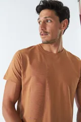 Remera color marrón con cuello redondo y manga corta. Presenta un estampado vertical con texto en japonés y líneas onduladas. Corte recto.