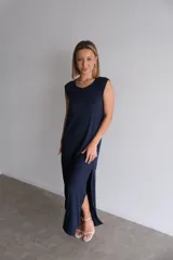 Vestido largo azul marino de tejido acanalado, con escote redondo y mangas cortas tipo hombrera. Presenta una abertura lateral en la falda.