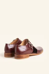 Zapato tipo oxford abierto en los laterales, confeccionado en cuero vacuno negro. Presenta doble tira con hebillas metálicas en el empeine y detalle de tachas plateadas en el contorno del talón y la puntera.