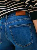 Jean ajustado de talle medio, color azul medio, con efecto desteñido en muslos y costuras, y efecto usado en la parte delantera. Presenta cierre de cremallera con botón y estilo de cinco bolsillos.