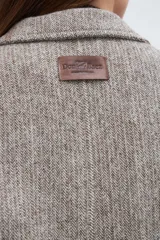 Saco corto entallado de lana fina, con cuello solapa, manga larga y cierre frontal con botones. Presenta un diseño clásico con textura de espiga en tonos tierra.