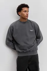 Buzo de cuello redondo en color gris oscuro con efecto lavado, manga larga y calce holgado. Presenta una pequeña estampa minimalista en el pecho.