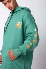 Buzo canguro oversize de algodón rústico, color gris claro, con capucha y cordones ajustables con logo estampado. Presenta un diseño gráfico pequeño en el pecho y detalles estampados en la manga.