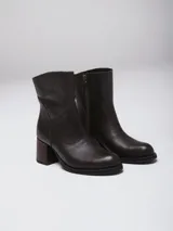 Botas de caña baja en cuero color marrón oscuro, con taco cuadrado y punta redondeada. Presentan un diseño tipo western con estribo desmontable que incluye una hebilla metálica decorativa.