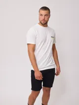 Remera blanca de algodón con cuello redondo y manga corta. Presenta un pequeño logo estampado en azul marino en el pecho izquierdo.