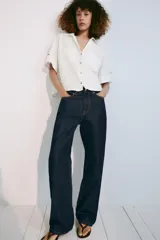 Camisa crop de mezcla de lino color blanco, con cuello solapa, escote en V, manga corta con trabilla, bolsillos de plastrón en el delantero y cierre frontal de botones.
