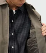 Campera de material sintético en color gris topo, con cuello inglés, cierre frontal por cremallera, mangas largas con puños elásticos y diseño de relieve tribal en la espalda.