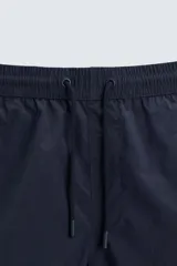 Short de baño de color azul marino, confeccionado en tejido técnico, con cintura elástica ajustable mediante cordón, bolsillos laterales y detalle de bolsillo trasero.