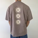Remera boxy de color marrón topo, de manga corta, con diseño estampado en la espalda de tres flores estilizadas en color blanco.