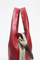 Bolso de mano grande Bimba y Lola modelo Paper, confeccionado en piel vacuna de color rojo. Presenta estructura blanda, asas de hombro fijas, tira lateral con mosquetón y detalle de logo metálico en la parte inferior.