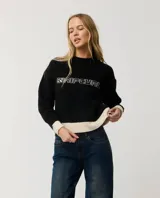 Buzo Rip Curl de punto color negro con diseño de bloques de color, presenta paneles en color crudo en los puños, cuello y el borde inferior. Incluye la inscripción "Rip Curl" bordada en el pecho con tipografía estilo gótico.