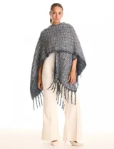 Ruana de tejido tipo tweed en tonos azul y gris con destellos de lurex. Presenta un diseño abierto con terminaciones desmechadas y flecos en todo el borde inferior.