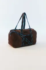 Bolso de viaje grande marrón de pana acolchada, con asas de hombro y tiras decorativas en tonos azules. Cuenta con cierre superior y una correa larga regulable.