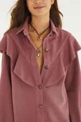 Camisa de denim color rosa viejo, con cuello clásico, volados grandes en el delantero, cierre frontal con botones y mangas largas con puños.
