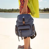 Mochila de nylon color bordó con tapa y broche metálico. Tiene apertura superior con broche, bolsillos internos, bolsillo con cierre metálico al frente y laterales. Incluye asas rígidas de mano y correas regulables para colgar en la espalda.