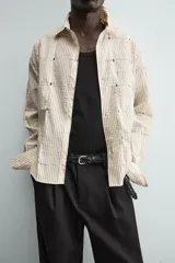 Camisa de corte relajado confeccionada en una mezcla de algodón y lino con textura semitransparente. Presenta un diseño de rayas verticales, cuello solapa, manga larga con puños abotonados y cierre frontal con botones.