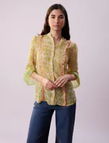 Blusa de gasa estampada con flores amarillas y verdes, marca Alex & Lili. Tiene cuello mao, mangas 3/4 acampanadas y cierre frontal con botones. Presenta volados verticales color naranja en el frente y en las mangas.