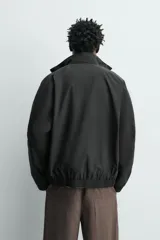 Cazadora bomber de corte relajado confeccionada en tejido técnico color negro. Presenta cuello subido, manga larga amplia, bolsillos de vivo en cadera, acabados elásticos y cierre frontal con cremallera de doble dirección.