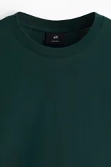 Remera de manga larga color verde oscuro, con cuello redondo ribeteado y corte estándar.