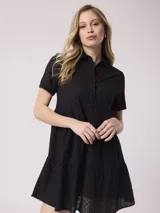 Vestido corto negro con cuello camisero, mangas cortas y falda escalonada con bordado broderie. Cierre frontal con botones.