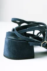 Sandalias de taco cuadrado medio, confeccionadas en gamuza color azul. Presentan tiras finas que cruzan el empeine, una pulsera ajustable al tobillo y detalle de cuentas decorativas en la tira frontal.