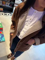 Campera de paño color marrón con diseño de botones frontales, bolsillos laterales y puños con vuelta en tejido de espiga bicolor. Presenta un corte holgado y estructura clásica.
