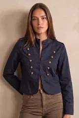 Chaqueta corta color beige de algodón, de inspiración militar con cuello mao y doble botonadura frontal con botones metálicos dorados.