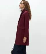 Abrigo largo de corte slim, color gris con textura jaspeada. Presenta solapas clásicas, cierre frontal con botones, bolsillos laterales con solapa y abertura trasera. Incluye forro interno.