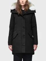 Campera negra de corte entallado, con capucha ajustable ribeteada en piel de coyote, cierre frontal con botones a presión y cremallera bidireccional, bolsillos laterales con solapa y puños acanalados.