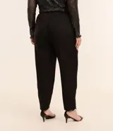 Pantalón zanahoria de vestir negro, con cintura alta, elástico en la espalda, bolsillos laterales, botón metalizado y pliegues delanteros.
