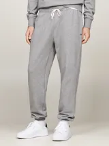 Pantalón de jogging gris de felpa de algodón, con cintura elástica ajustable con cordón, dos bolsillos laterales, un bolsillo trasero y bajos elásticos. Presenta el logo de Tommy Hilfiger bordado en el lateral.