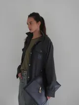 Camisa de lana color gris oscuro, de corte clásico con bolsillos frontales con solapa, cuello camisero y cierre frontal con botones.
