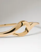 Pulsera rígida tipo brazalete PDPAOLA modelo Brise, chapada en oro, con un diseño fluido y entrelazado que forma un nudo central.
